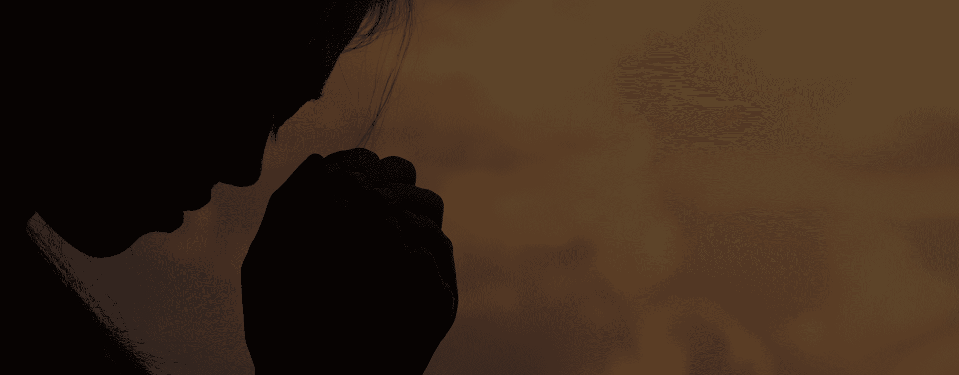 Silhouette of a person praying with hands clasped at sunset