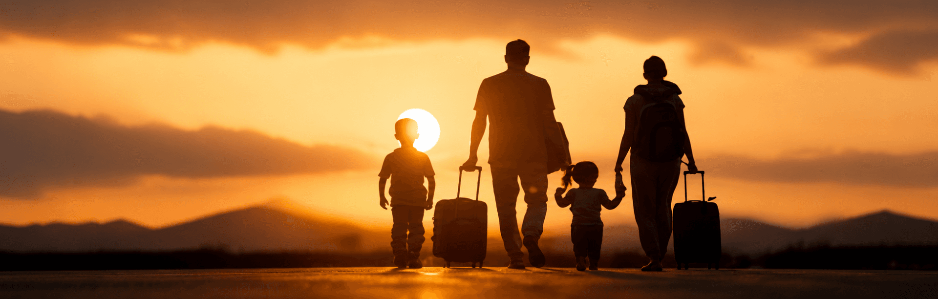 A family of four walking through an airport at sunset, pulling suitcases